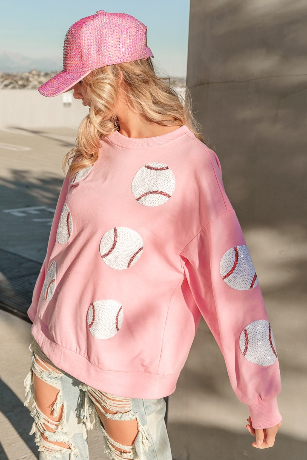 Person wearing a trendy and eye-catching pink sequin cap and the BiBi Sequin Baseball Patches French Terry Sweatshirt, standing in outdoor daylight.