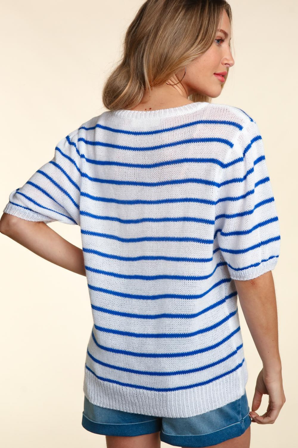 A woman wearing a chic Haptics Letter Embroidery Striped Knit Top featuring "America" in red stands against a neutral background. The white and blue striped knit design pairs perfectly with her denim shorts.