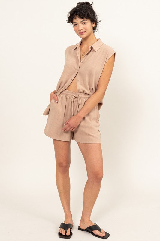 Against a beige backdrop, a woman effortlessly embodies summer style in the Linen Shirt and Shorts Set, featuring a relaxed fit that exudes chic simplicity.