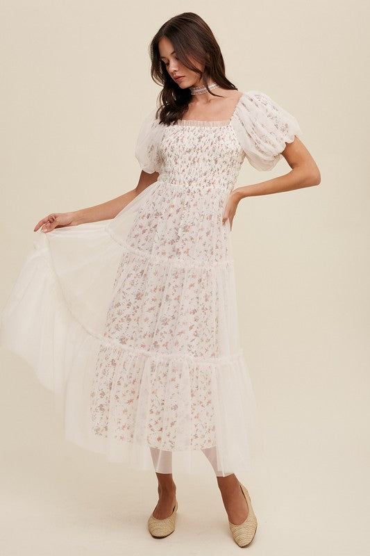 A woman in a Floral Print and Mesh Puff Sleeve Maxi Dress stands against a plain background, looking slightly to the side.