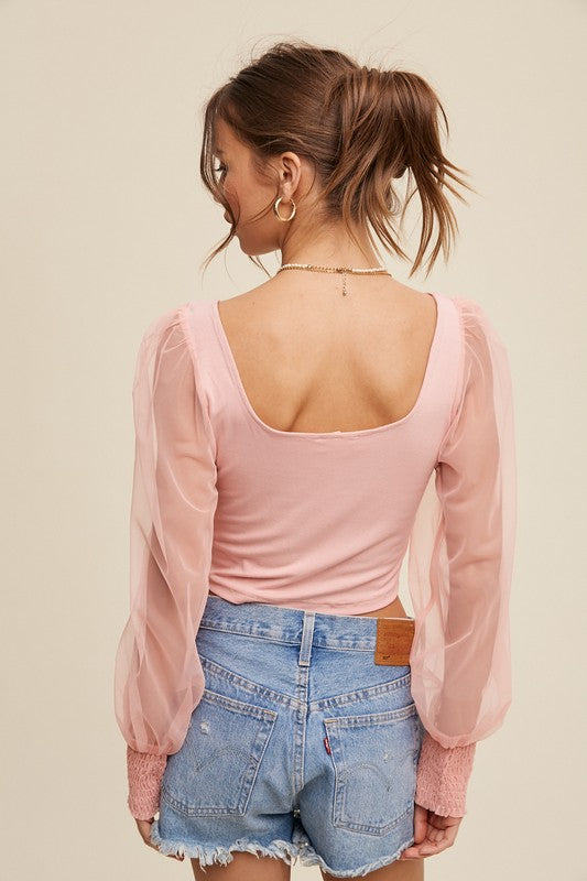 A woman with brown hair tied back wears the *Square Neck Mesh Puff Sleeve Knit Top* in light pink, paired with blue jeans. She accessorizes with gold hoop earrings and a necklace while standing in front of a neutral background.