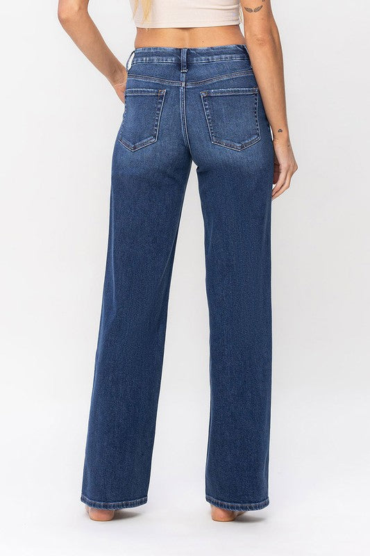 A person stands barefoot against a plain background, wearing a sleeveless top and the High Rise Loose Fit Jeans. These blue wide-leg jeans provide a loose fit that exudes comfort and effortless style.