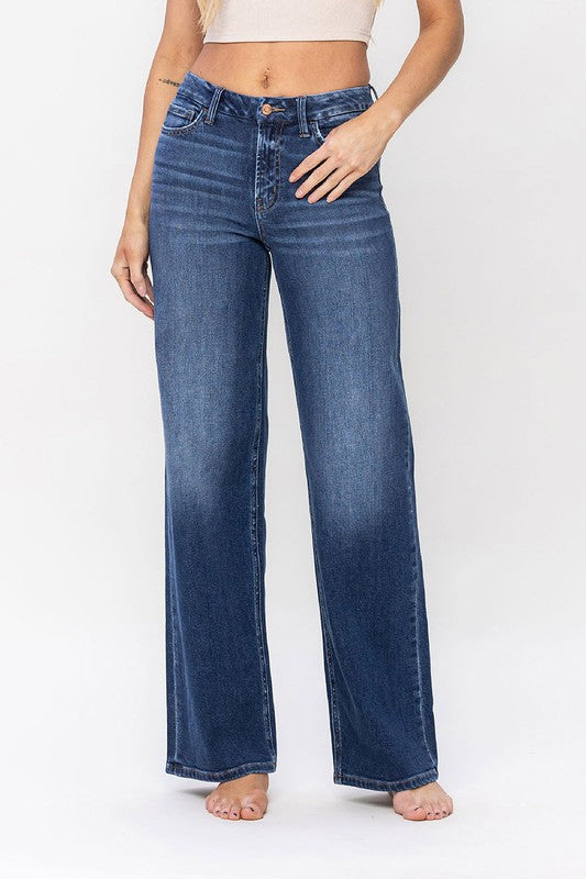 A person stands barefoot against a plain background, wearing a sleeveless top and the High Rise Loose Fit Jeans. These blue wide-leg jeans provide a loose fit that exudes comfort and effortless style.