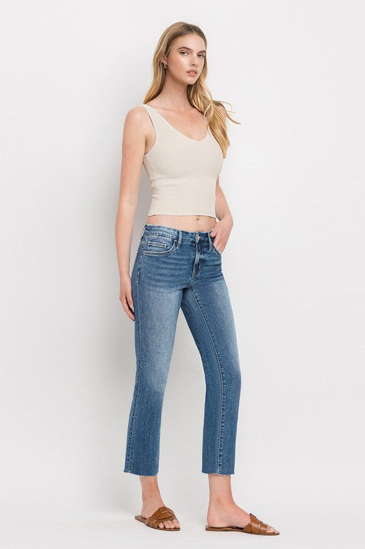 Individual styled in Mid Rise Crop Slim Straight Jeans, featuring a blue hue and frayed hems, paired with a white cropped top and complemented by brown open-toe sandals.