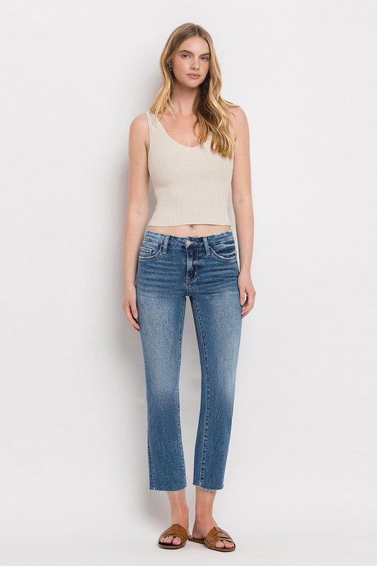 Individual styled in Mid Rise Crop Slim Straight Jeans, featuring a blue hue and frayed hems, paired with a white cropped top and complemented by brown open-toe sandals.