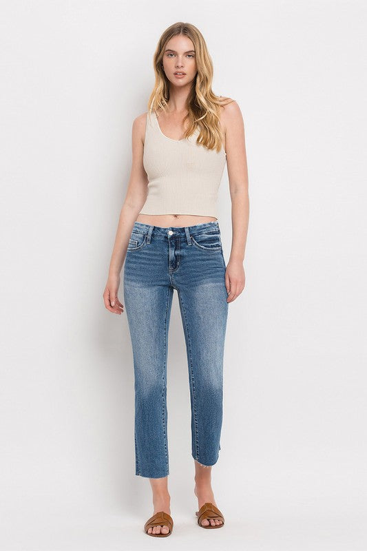 Individual styled in Mid Rise Crop Slim Straight Jeans, featuring a blue hue and frayed hems, paired with a white cropped top and complemented by brown open-toe sandals.