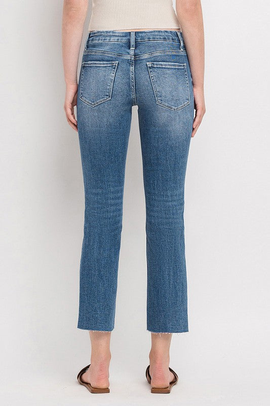 Individual styled in Mid Rise Crop Slim Straight Jeans, featuring a blue hue and frayed hems, paired with a white cropped top and complemented by brown open-toe sandals.