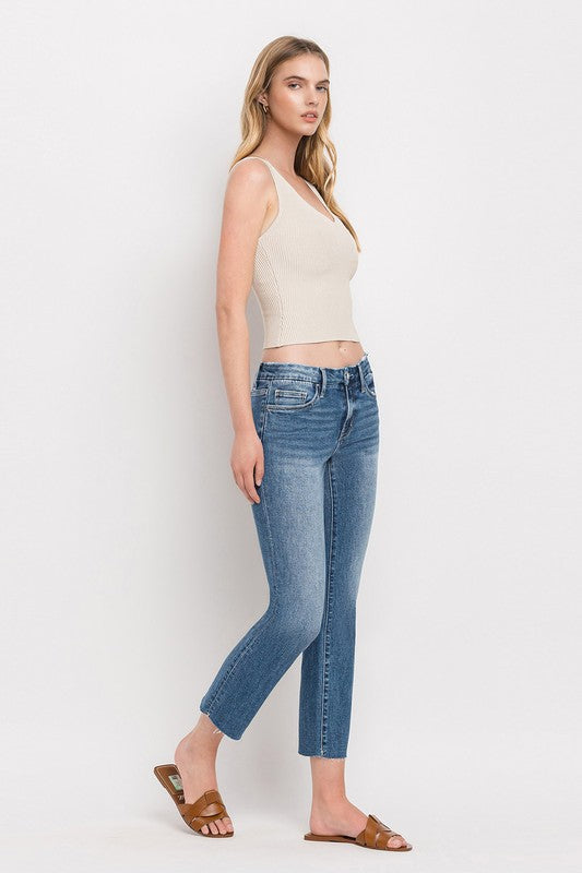 Individual styled in Mid Rise Crop Slim Straight Jeans, featuring a blue hue and frayed hems, paired with a white cropped top and complemented by brown open-toe sandals.