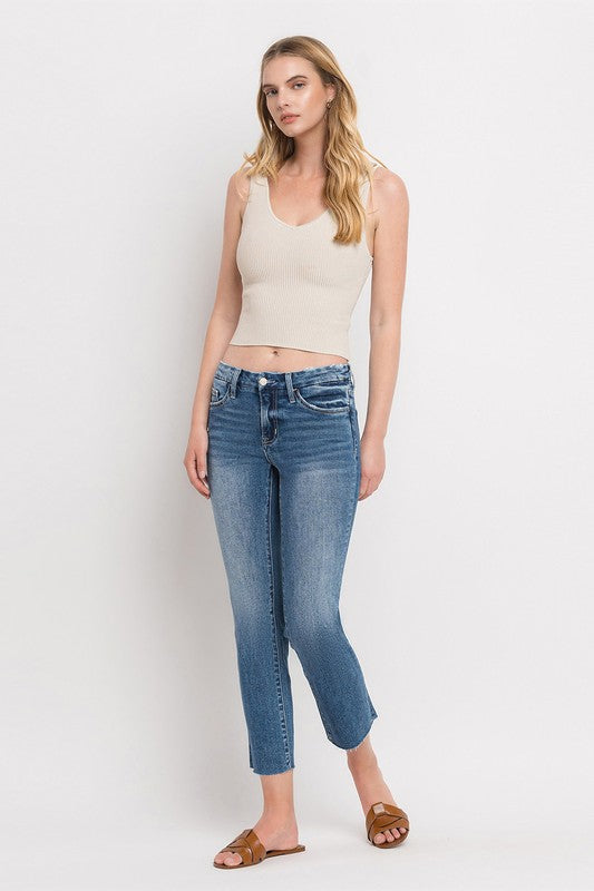 Individual styled in Mid Rise Crop Slim Straight Jeans, featuring a blue hue and frayed hems, paired with a white cropped top and complemented by brown open-toe sandals.