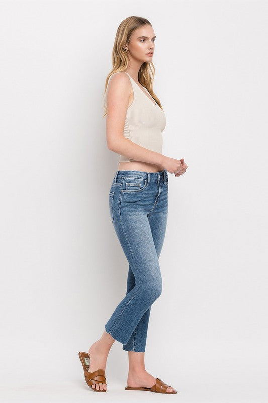 Individual styled in Mid Rise Crop Slim Straight Jeans, featuring a blue hue and frayed hems, paired with a white cropped top and complemented by brown open-toe sandals.