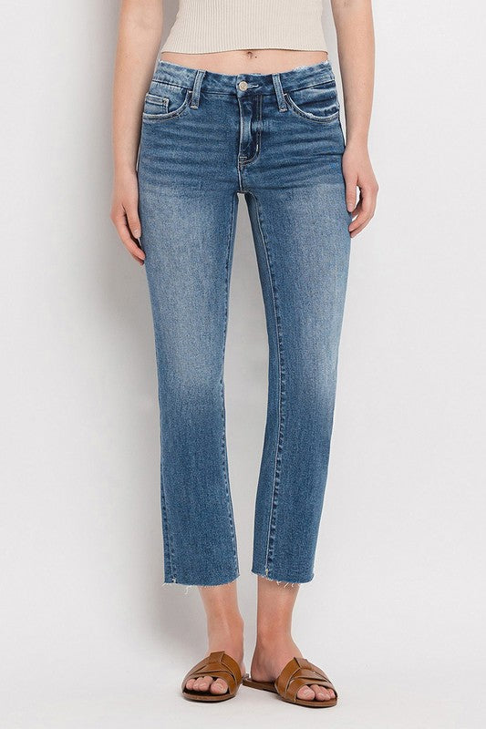 Individual styled in Mid Rise Crop Slim Straight Jeans, featuring a blue hue and frayed hems, paired with a white cropped top and complemented by brown open-toe sandals.