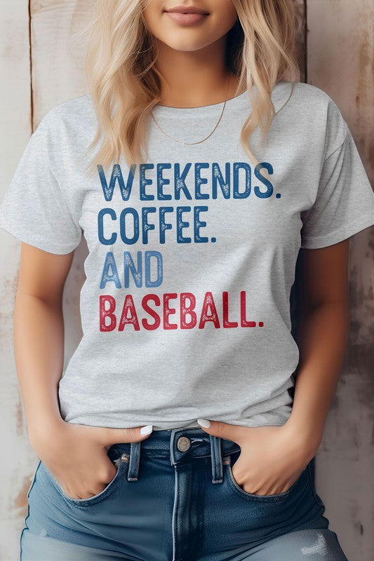 A person with blonde hair stands against a wooden background, wearing the Weekends. Coffee. and Baseball Graphic Tee, showcasing its bold blue and red lettering that proudly states "WEEKENDS. COFFEE. AND BASEBALL.