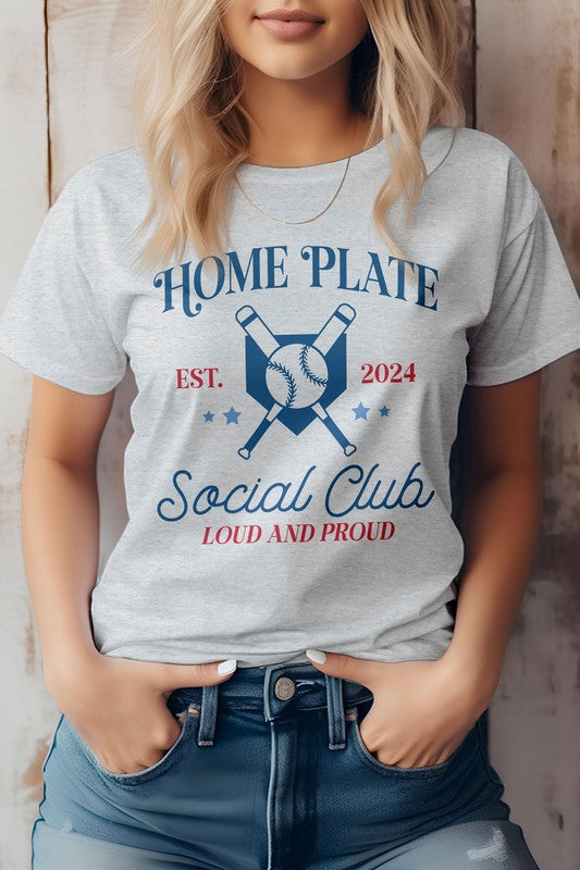 Person wearing a white "Home Plate, Social Club, Baseball Graphic Tee" featuring crossed bats and a baseball graphic, along with "EST. 2024" and "LOUD AND PROUD" text, paired with blue jeans.