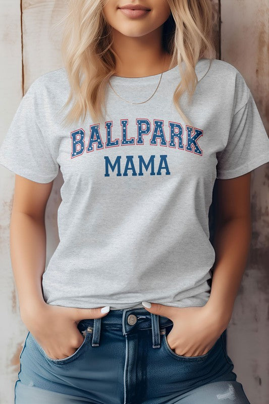 A person wearing a light gray Ballpark MAMA Baseball Graphic Tee has blonde hair and is standing with their hands in the pockets of blue denim jeans, effortlessly showcasing casual sports apparel.