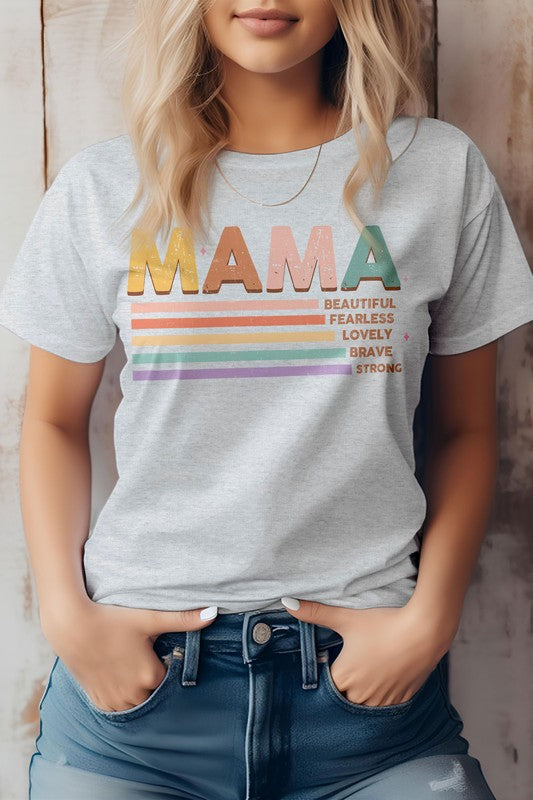 A person wearing the MAMA Graphic Tee, a beige shirt featuring the word "MAMA" in colorful letters and descriptions like "Beautiful," "Fearless," "Lovely," "Brave," and "Strong" written below—perfect for Mother's Day.