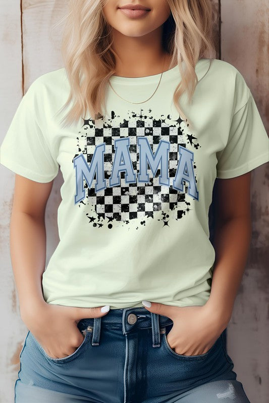 Person wearing the Mama Retro Checkered Rocker Mom Graphic Tee, a light gray T-shirt featuring the words "MAMA" in blue letters over a black and white checkered design, evoking that mama retro checkered rocker mom vibe. Hands in pockets, standing against a wooden backdrop. Perfect for Mother's Day with its high-quality print.