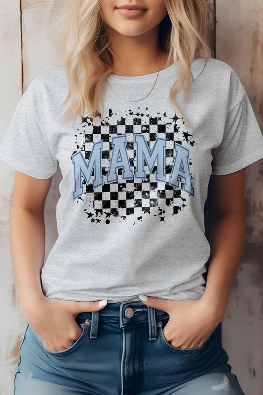 Person wearing the Mama Retro Checkered Rocker Mom Graphic Tee, a light gray T-shirt featuring the words "MAMA" in blue letters over a black and white checkered design, evoking that mama retro checkered rocker mom vibe. Hands in pockets, standing against a wooden backdrop. Perfect for Mother's Day with its high-quality print.