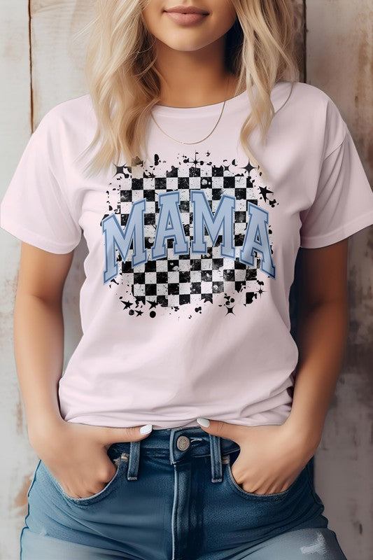 Person wearing the Mama Retro Checkered Rocker Mom Graphic Tee, a light gray T-shirt featuring the words "MAMA" in blue letters over a black and white checkered design, evoking that mama retro checkered rocker mom vibe. Hands in pockets, standing against a wooden backdrop. Perfect for Mother's Day with its high-quality print.