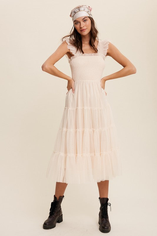 A woman in a Smocked Ruffle Tiered Mesh Midi Maxi Dress, featuring mauve tulle layers with smocked ruffles and ruffled straps, poses against a plain background. She is accessorized with long earrings and silver heels.