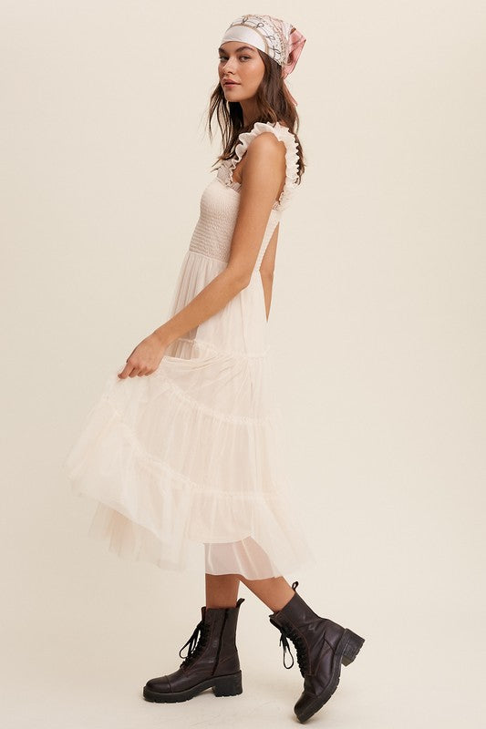 A woman in a Smocked Ruffle Tiered Mesh Midi Maxi Dress, featuring mauve tulle layers with smocked ruffles and ruffled straps, poses against a plain background. She is accessorized with long earrings and silver heels.