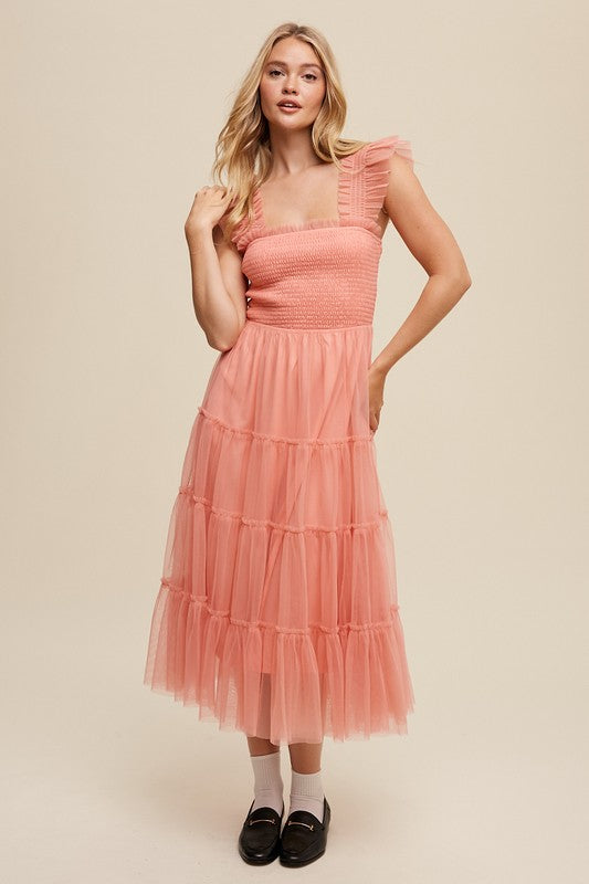 A woman in a Smocked Ruffle Tiered Mesh Midi Maxi Dress, featuring mauve tulle layers with smocked ruffles and ruffled straps, poses against a plain background. She is accessorized with long earrings and silver heels.