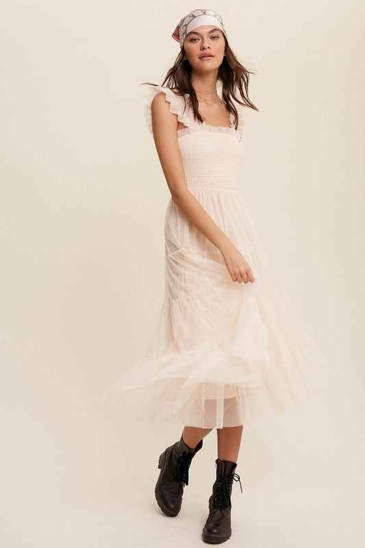 A woman in a Smocked Ruffle Tiered Mesh Midi Maxi Dress, featuring mauve tulle layers with smocked ruffles and ruffled straps, poses against a plain background. She is accessorized with long earrings and silver heels.