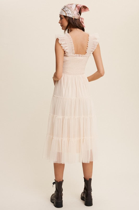 A woman in a Smocked Ruffle Tiered Mesh Midi Maxi Dress, featuring mauve tulle layers with smocked ruffles and ruffled straps, poses against a plain background. She is accessorized with long earrings and silver heels.