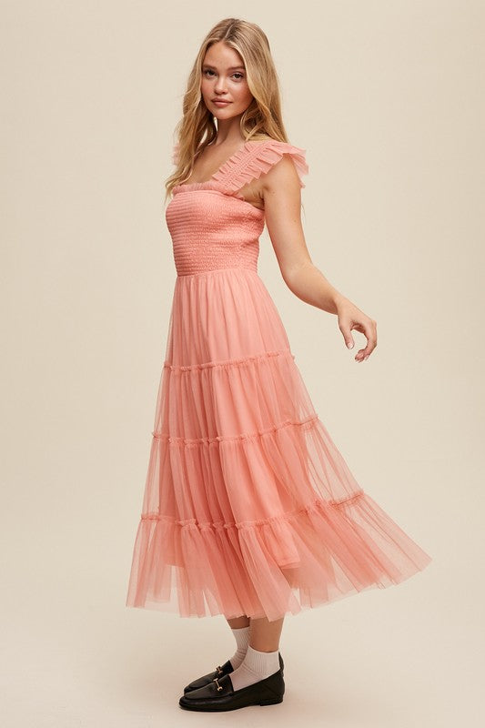 A woman in a Smocked Ruffle Tiered Mesh Midi Maxi Dress, featuring mauve tulle layers with smocked ruffles and ruffled straps, poses against a plain background. She is accessorized with long earrings and silver heels.