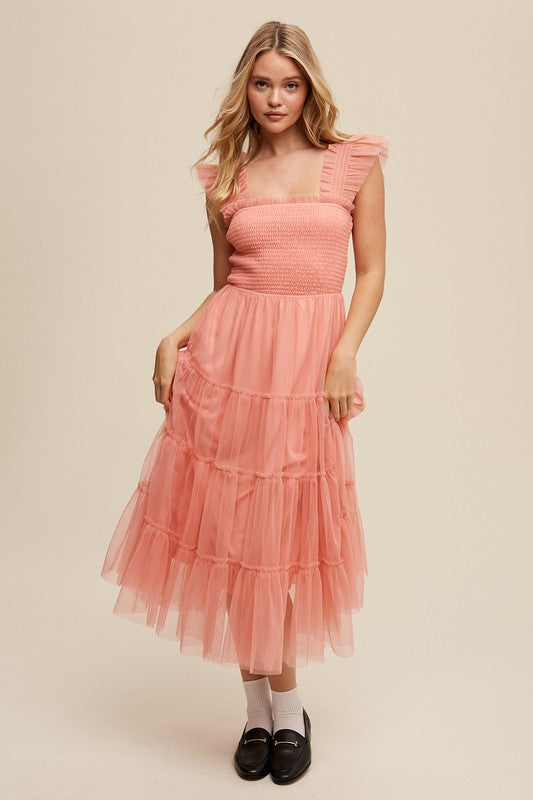 A woman in a Smocked Ruffle Tiered Mesh Midi Maxi Dress, featuring mauve tulle layers with smocked ruffles and ruffled straps, poses against a plain background. She is accessorized with long earrings and silver heels.