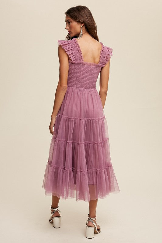 A woman in a Smocked Ruffle Tiered Mesh Midi Maxi Dress, featuring mauve tulle layers with smocked ruffles and ruffled straps, poses against a plain background. She is accessorized with long earrings and silver heels.