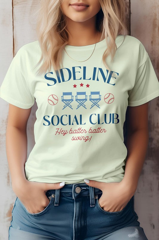 A person is wearing the Sideline Social Club Baseball Graphic Tee, displaying the words "Hey batter batter swing!" alongside images of two baseballs and three director's chairs. This white T-shirt features a unisex fit, making it an ideal choice for any baseball fan.