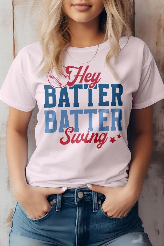 A person wearing the Hey Batter Batter Swing, Baseball Graphic Tee which has "Hey Batter Batter Swing" written in red and blue letters along with a small baseball graphic above the text on a white t-shirt. Made in the USA from eco-friendly materials, this tee is perfect for any fan of baseball.