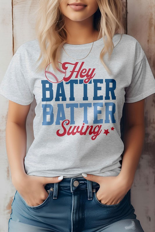 A person wearing the Hey Batter Batter Swing, Baseball Graphic Tee which has "Hey Batter Batter Swing" written in red and blue letters along with a small baseball graphic above the text on a white t-shirt. Made in the USA from eco-friendly materials, this tee is perfect for any fan of baseball.