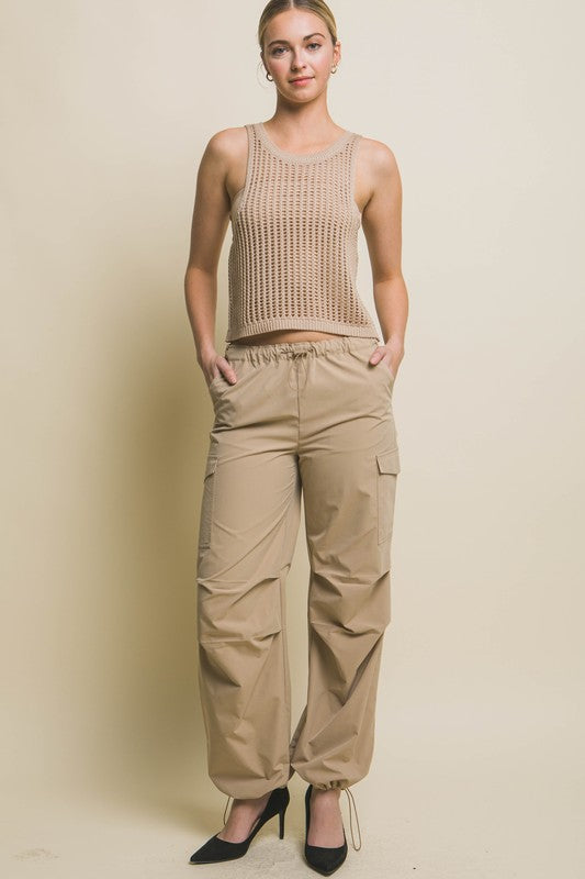 A person poses in a beige Sleeveless Open Knit Crop Top paired with tan drawstring pants against a light background.