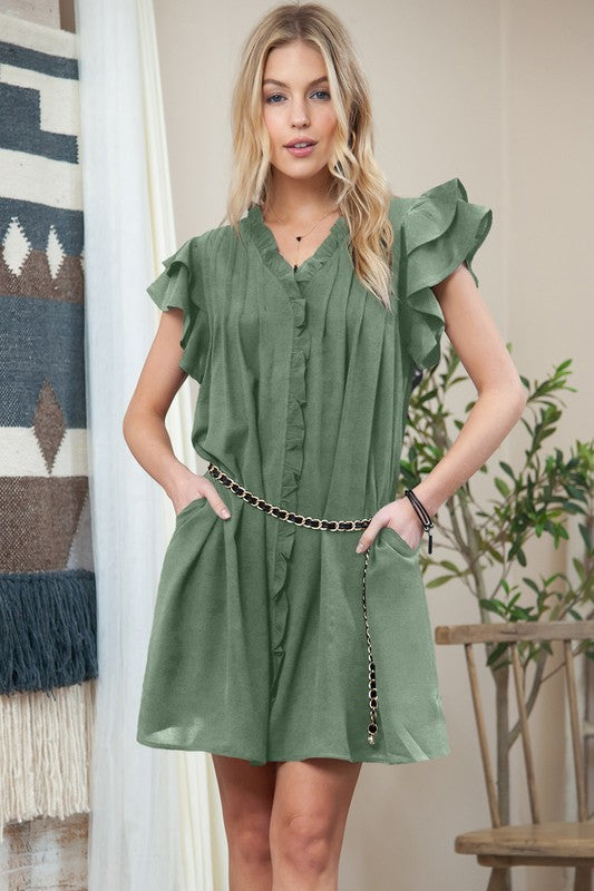 Woman in a green Ruffle Sleeve V Neck dress with pockets, standing against a peach-colored wall, smiling with hands on hips.