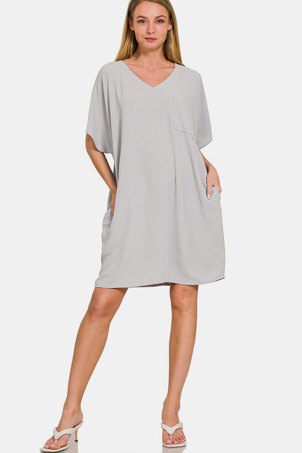 A person wearing the versatile light gray Zenana V-Neck Tee Dress with a chest pocket and a side pocket.