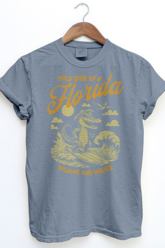 The Florida's Wild Side, Retro Vintage Garment Dye Tee is a gray t-shirt with a hanging loop, featuring a vintage wash graphic of an alligator riding a wave along with the text "Wild side of Florida" and "Wildlife and Waves" in a retro font.