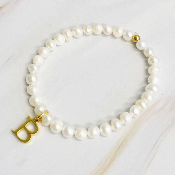 An assortment of Freshwater Pearl Initial Charm Bracelets displayed on a marble surface.