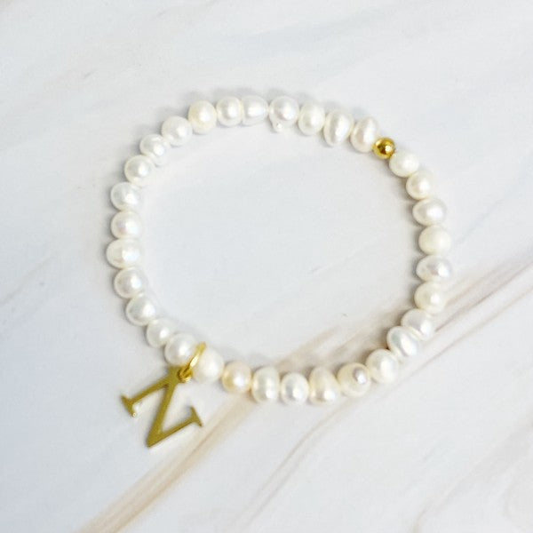 An assortment of Freshwater Pearl Initial Charm Bracelets displayed on a marble surface.
