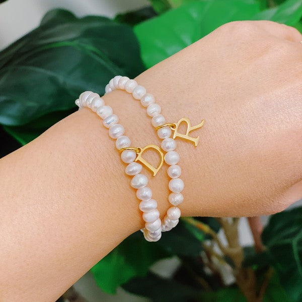 An assortment of Freshwater Pearl Initial Charm Bracelets displayed on a marble surface.