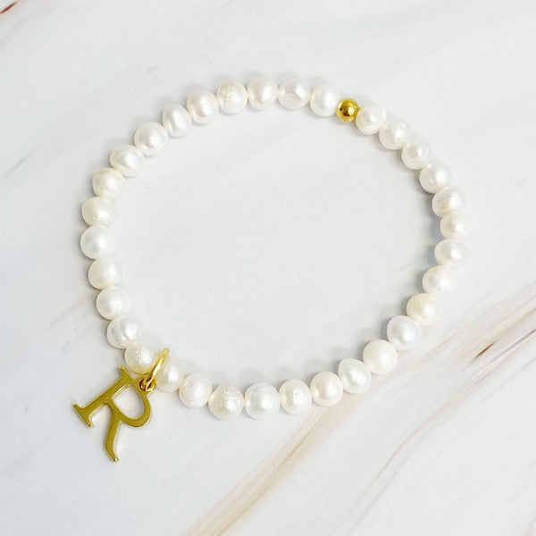 An assortment of Freshwater Pearl Initial Charm Bracelets displayed on a marble surface.