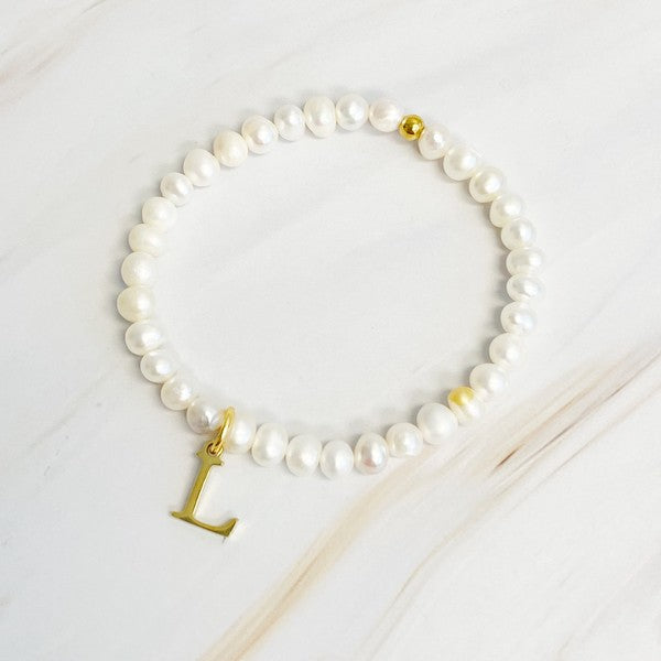 An assortment of Freshwater Pearl Initial Charm Bracelets displayed on a marble surface.