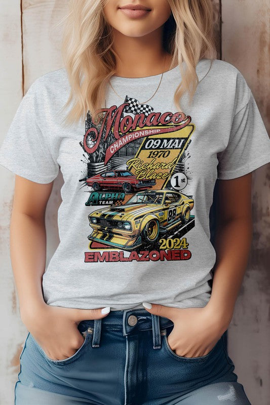 A person sporting a white Emblazoned Race Retro Vintage Graphic Tee, showcasing a vintage race car, the word "Monaco," and the date "09 May 1970." Crafted from eco-friendly materials, the shirt also features the text "Emblazoned" and the year "2024.