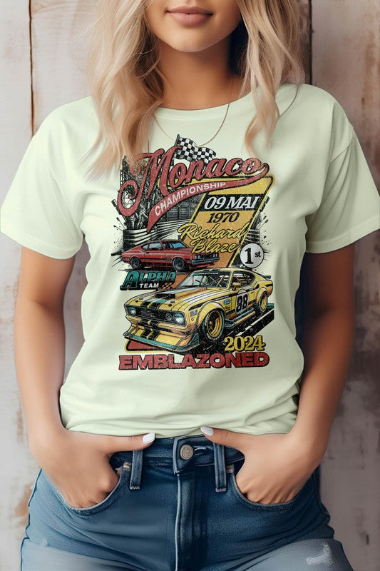 A person sporting a white Emblazoned Race Retro Vintage Graphic Tee, showcasing a vintage race car, the word "Monaco," and the date "09 May 1970." Crafted from eco-friendly materials, the shirt also features the text "Emblazoned" and the year "2024.