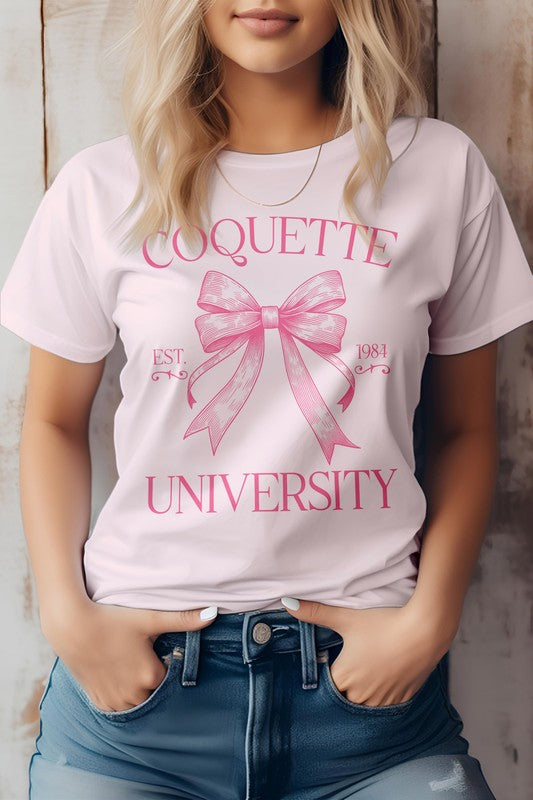 A person is wearing the Vintage Coquette University Graphic Tee made from combed and ring-spun cotton, featuring the text "Coquette University" and a bow graphic along with "Est. 1984." The individual stands with hands in the pockets of blue jeans.