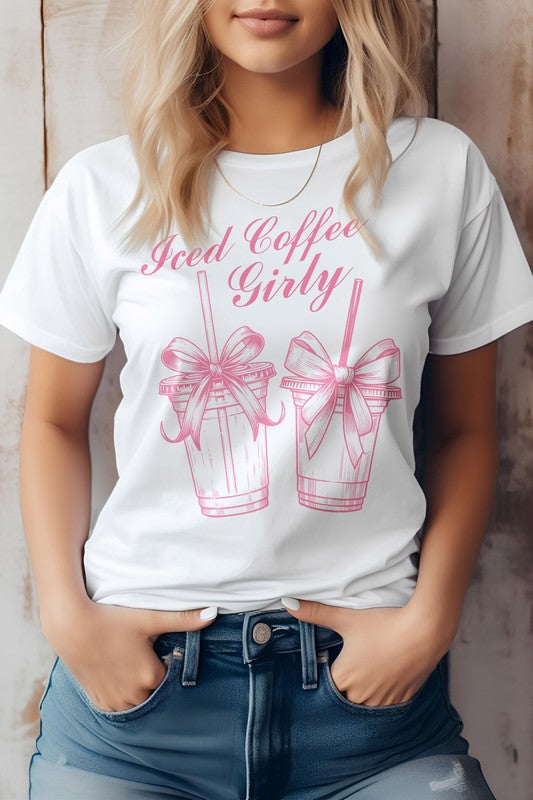 A woman wearing a Vintage Coquette Coffee Graphic Tee, made from eco-friendly materials, poses with her hands in her jean pockets. Her gray t-shirt features the text "Iced Coffee Girly" and graphic images of two iced coffee cups with bows.