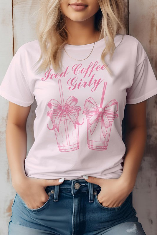 A woman wearing a Vintage Coquette Coffee Graphic Tee, made from eco-friendly materials, poses with her hands in her jean pockets. Her gray t-shirt features the text "Iced Coffee Girly" and graphic images of two iced coffee cups with bows.