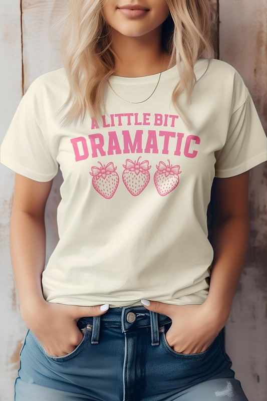 Person wearing a Vintage Coquette Strawberry Graphic Tee, featuring the text "A Little Bit Dramatic" and three illustrated strawberries below it, stands with hands in jean pockets. This stylish Bella Canvas tee is crafted from eco-friendly materials for a sustainable fashion choice.