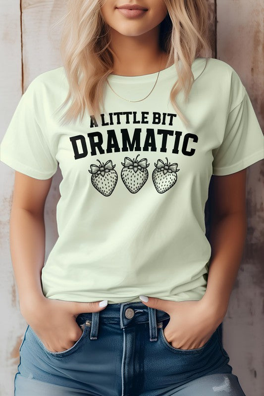 Person wearing a Vintage Coquette Strawberry Graphic Tee, featuring the text "A Little Bit Dramatic" and three illustrated strawberries below it, stands with hands in jean pockets. This stylish Bella Canvas tee is crafted from eco-friendly materials for a sustainable fashion choice.