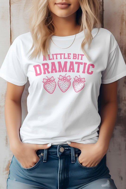 Person wearing a Vintage Coquette Strawberry Graphic Tee, featuring the text "A Little Bit Dramatic" and three illustrated strawberries below it, stands with hands in jean pockets. This stylish Bella Canvas tee is crafted from eco-friendly materials for a sustainable fashion choice.